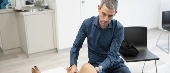 Ein Hausarzt untersucht eine Patientin mit Knieschmerzen. - © picture alliance/KEYSTONE