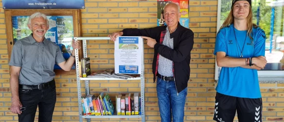 Wolfgang Kohl und Peter Schindel vom Förderverein der Stadtbibliothek Detmold übergeben das gespendete Bücherregal in Berlebeck an Toni Lause, Fachangestellter für Bäderbetriebe (von links). - © Stadt Detmold