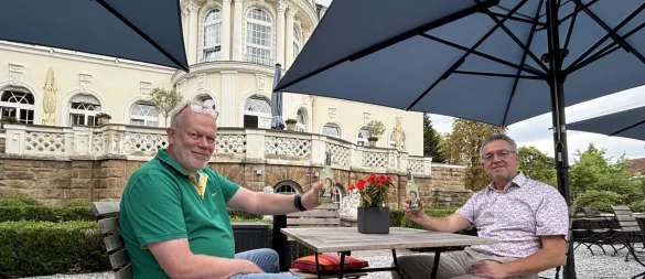 Jupp Westfeld, Cheforganisator der Sommer-Radl-Sause (links), und Andreas Gerbig, Direktor der "Villa Dürkopp", stoßen mit einer Salzufler Sole-Limo auf die Sommer-Radl-Sause an, die am 7. September auch in dem Biergarten am Fuß der Gründerzeit-Fassade Station macht. - © Thomas Reineke