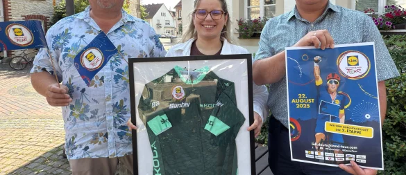 Mobilitätsmanager Henning Schwarze und Bürgermeister Marcus Püster bereiten das Streckenfest vor und freuen sich, dass die Naturparkkommune Schlangen Etappenort ist. Auszubildende Michelle Geppert präsentiert das Trikot von Radstar Jonathan Milan. - © Gemeinde Schlangen