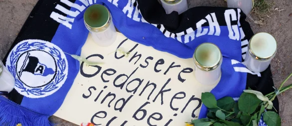 Unsere Gedanken sind bei Euch!, ist am Tatort in Messer-Anschlags in Bielefeld zu lesen. Fans haben Kerzen und Schal für die Opfer niedergelegt. - © Friso Gentsch/dpa