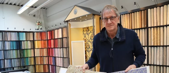 Gert Prüßner steht in seinem Teppichboden-Studio und blättert am Kollektionstisch durch verschiedene Tapetenmotive. Neben den beliebten Digitaldruck-Fototapeten sind besonders die duftenden Tapeten aus Österreich ein Hingucker – ihre Oberflächen bestehen aus getrocknetem Heu oder Kornblumen. Foto: Anna Lena Hinder - © Anna Lena Hinder