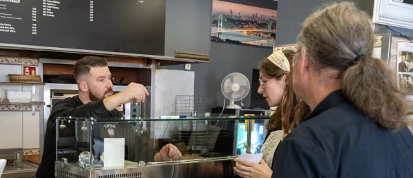 Matthias Zizelmann (rechts) und Mona Lorenz von HBM Chribal übergeben Tafel und Plakate für die Aktion „Miteinander, Füreinander“ an Mesut Ocak von Taksim Pizza & Döner. - © Stadt Horn-Bad Meinberg