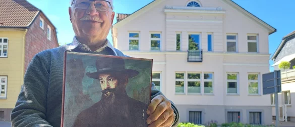 Dr. Hans-Joachim Keil präsentiert die Abbildung eines Porträts von Adolf Neumann-Hofer vor dessen ehemaligen Wohnhaus in der Leopoldstraße. Das Gemälde stammt vom Künstler Bruno Wittenstein (1876-1968), ist um 1920 mit Öl auf Leinwand entstanden und zeigt Adolf Neumann-Hofer mit seinem Markenzeichen: dem langen, dunklen Bart. - © Carolin Brokmann-Förster