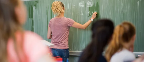Eine junge Lehrerin schreibt eine Matheaufgabe an die Tafel. Der Pädagogen-Nachwuchs in NRW ist ein heikles Thema. - © picture alliance / Julian Stratenschulte/dpa