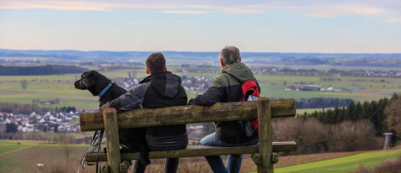 Wanderer sitzen mit einem Hund auf einer Bank am Waldrand. In den Wäldern in OWL müssen immer wieder Bänke abgebaut werden. - © picture alliance/dpa