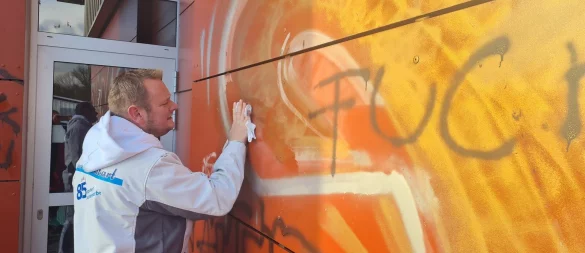 Mühevolle Kleinarbeit: Malermeister Falk Hötger probiert es erst mal mit Lösungsmittel, um die Schmiererei an der Wand über dem Flachdach zu entfernen. Bei Gold und Schwarz klappt das zunächst ganz gut, das Silber ist hartnäckig. - © Marianne Schwarzer