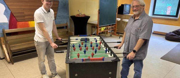 Tim Alexander (links) und Axel Schwarze laden Kinder und Jugendliche zum Mitmachen ein. Hier stehen sie am Kicker in der Trinitatiskirche in Schötmar. - © Sven Kienscherf