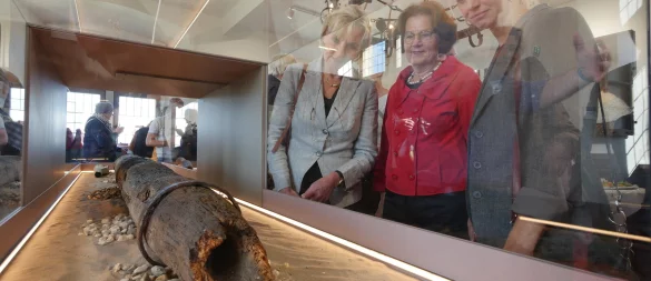 Dr. Ute Röder (NRW-Stiftung, von links), Anne Oelers-Albertin (Heimatverein Horn) und Dr. Stella Junger-Schwenner (stellvertretende Bürgermeisterin) schauen sich die neue Präsentation des Holz-Wasserrohrs im Roten Saal des Burgmuseums an. - © Jost Wolf