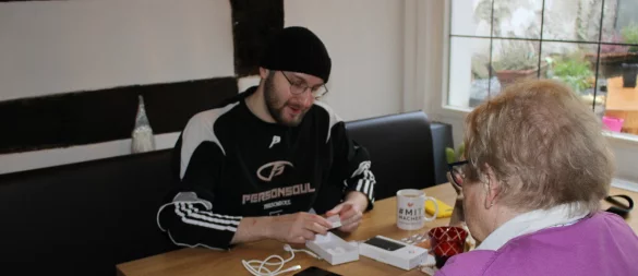 Winston Linford von der Volkshochschule erklärt einer Seniorin das Übertragen von Daten auf ihr neues Handy. - © Raffael Giebel