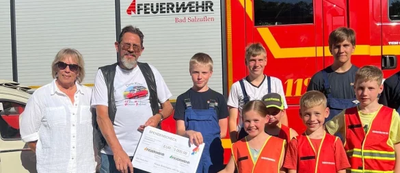 Oldtimer-Fan Klaus Siekmann übergibt einen symbolischen Spendenscheck an die Gruppe 1 der Jugendfeuerwehr Holzhausen. Links steht Siekmanns Lebensgefährtin Petra Werner. - © Klaus Siekmann