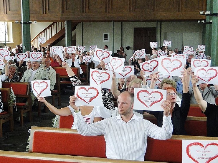 Die Kirchenbesucher halten beim Abschiedsgottesdienst für Pfarrer Rainer Stecker kleine Schilder mit der herzlichen Aufschrift "Wir werden Sie vermissen" in die Höhe. - © Foto: Karenfeld