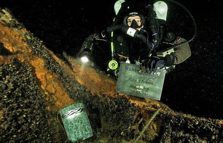 Matthias Schneider legt Urne und Gedenktafel am Heck des Schiffswracks ab. Die Urne hat er so verkeilt, dass die Bewegung des Wassers sie nicht fortreißen kann. Am Wrack sind die unzähligen Miesmuscheln gut zu erkennen. - © FOTO: ANDREAS KLOFT
