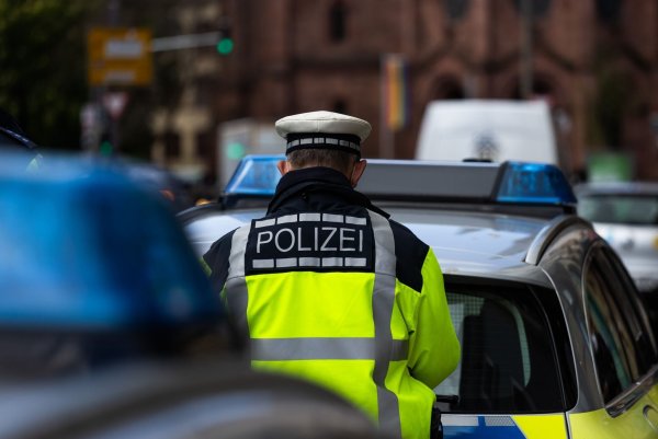 Ein Polizeibeamter steht zwischen zwei Einsatzfahrzeugen der Polizei. - © Philipp von Ditfurth/dpa/Symbolbild