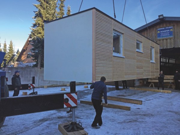 Schwebt: Das erste Modul des Containers wird mit Hilfe eines Krans außerhalb der Halle platziert. - © Henning Schwarze