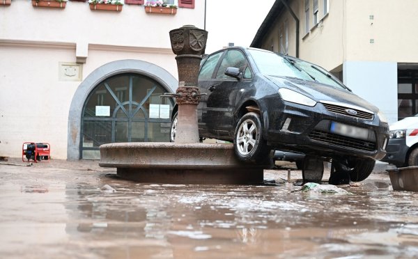 Auf einem Brunnen in Rudersberg hängt ein durch das Hochwasser weggespültes Auto. - © dpa