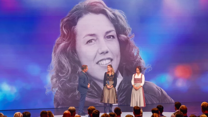 Die Biathletinnen Franziska Preuß und Magdalena Neuner (hier mir Moderator Markus Othmer vor einem Bild von Laura Dahlmeier) haben bei der Verleihung des Bayerischen Sportpreises ihrer gestorbenen Kollegin Dahlmeier gedacht. - © Alexandra BEIER/BayStMI/dpa