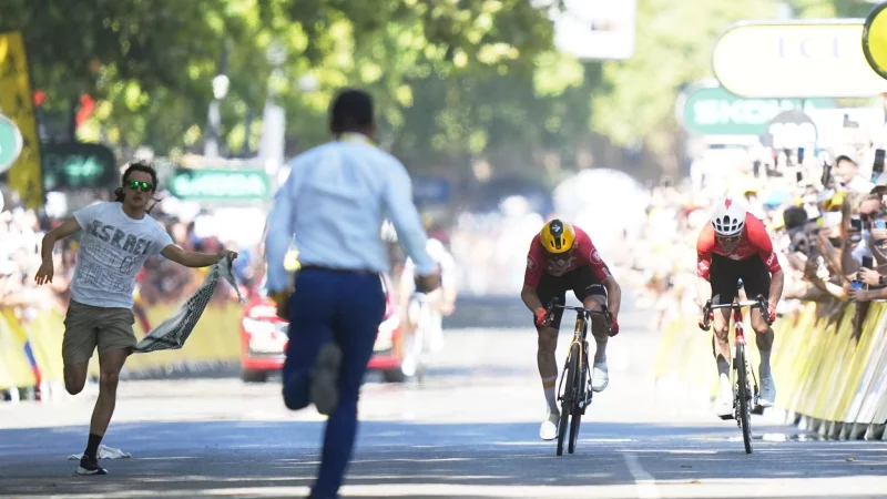 Während Jonas Abrahamsen und Mauro Schmid (r) in Toulouse um den Sieg sprinten, läuft ein Flitzer (l) auf die Zielgerade. - © Thibault Camus/AP/dpa