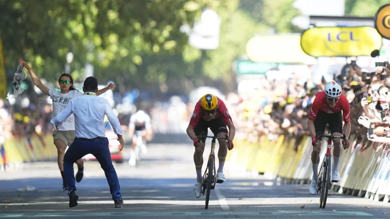 Ein Sicherheitsbeamter drängt in Toulouse einen Flitzer von der Zielgeraden, während Jonas Abrahamsen und Mauro Schmid um den Sieg sprinten. - © Thibault Camus/AP/dpa