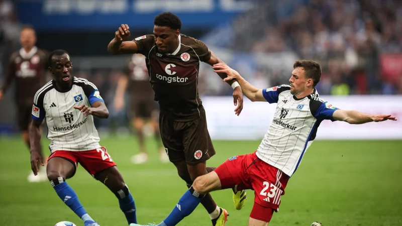 Voll dabei: St. Paulis Oladapo Afolayan (M) kämpft mit Hamburgs Jean-Luc Dompe (l) und Hamburgs Jonas Meffert um den Ball. (Archiv) - © Christian Charisius/dpa