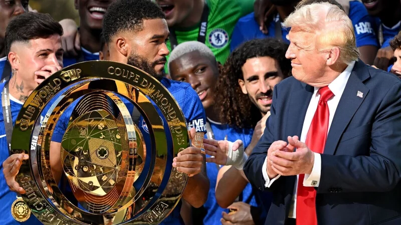 Chelseas Kapitän Reece James (l/vorn) hält auf dem Siegerpodest die Trophäe in den Händen und schaut irritiert zu US-Präsident Donald Trump. - © Sven Hoppe/dpa