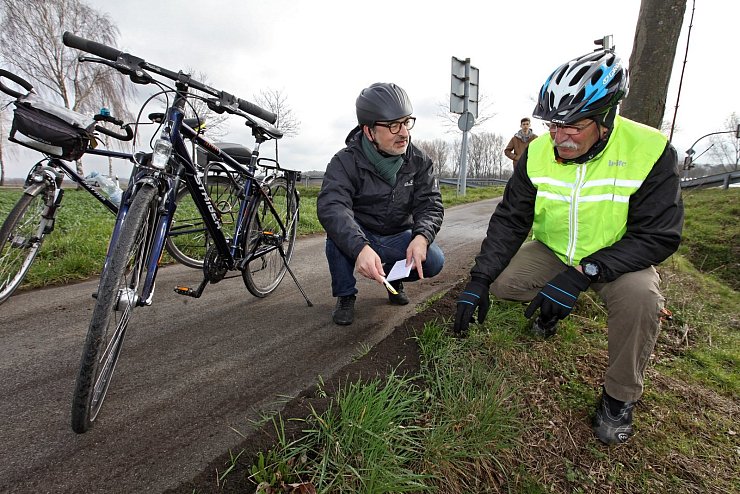 Auf dem Radweg am Hellweg gibt es Absenkungen, in denen sich Wasser, Eis und Schlamm ansammelt. Hagen Fiebig (mit Weste) zeigt Erol Kamisli: Schneisen helfen, damit Wasser ablaufen kann. - © Bernhard Preuß