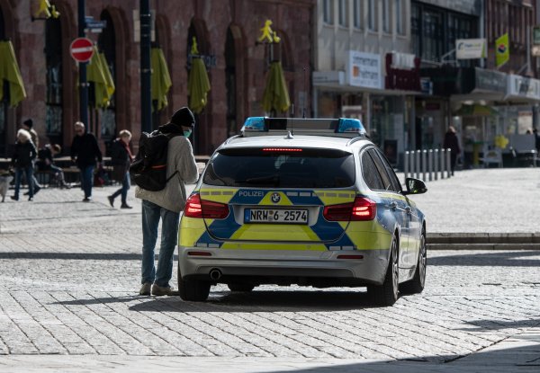 Ein Mann mit einem Mundschutz unterhält sich in der Fußgängerzone mit den Polizisten in einem Streifenwagen. Nordrhein-Westfalen hat einen Bußgeldkatalog für Verstöße gegen die landesweiten Corona-Regeln mit Strafen bis zu 5000 Euro erlassen. - © Bernd Thissen/dpa