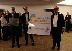 Bürgermeister Macus Baier (von links), Oberst Jörg Mayer und Major Daniel Becker zeigen die Tafel mit dem Logo „Immaterielles Kulturerbe“. - © Laura Meya