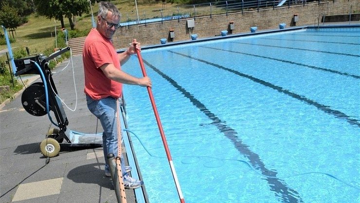 Schwimmmeister Dirk Seifert reinigt den Beckenrand mit dem langen Besen. - © Karin Prignitz