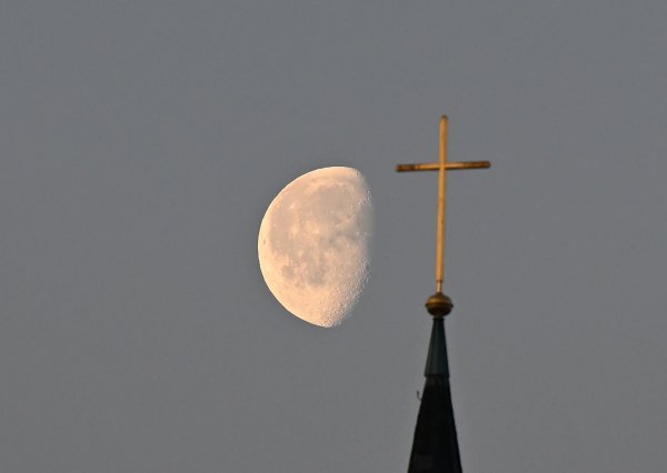Der Mond steht im Morgenlicht hinter einem Kreuz auf einem Kirchturm. - © Bernd Weißbrod/dpa/Symbolbild