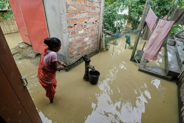 Eine Frau versucht in der überfluteten Umgebung ihres Hauses, Wasser zu sammeln. - © Uncredited/AP/dpa