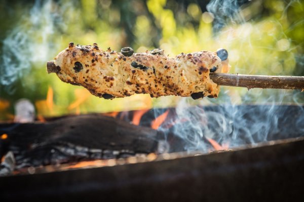 Ein Oliven-Feta-Knoblauch-Hefeteig ist um einen Haselnuss-Stock gewickelt und wird über dem Lagerfeuer gebacken. - © Christin Klose/dpa-tmn