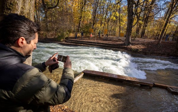 Freizeitsurfer Alexander Neumann fotografiert die - zurzeit nicht funktionstüchtige - Eisbachwelle im Englischen Garten. - © Peter Kneffel/dpa