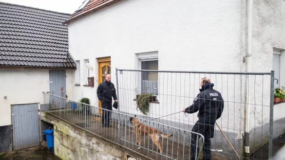 Ermittlungen vor Ort: Ein Polizist mit einem Hund an der Leine auf dem Grundstück vor dem Haus des beschuldigten Ehepaares in Höxter-Bosseborn. - © dpa