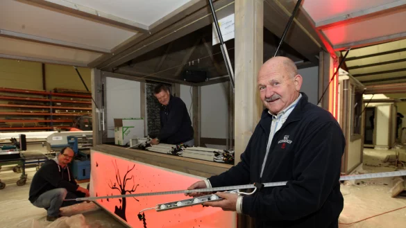 Neues Licht: Heinz Holey (rechts) zeigt die neuen, schlanken LED-Leistenim Vergleich zu den alten, kurzen Elementen. Die neue Beleuchtung soll die Hütten in wärmerem Weiß oder intensiveren Farbtönen leuchten lassen als im vergangenen Jahr. Im Bildhintergrund arbeiten Wolfgang Kirstein von der Werbegemeinschaft (Mitte) und Marcus Zauner von der Firma LEDtecam Beleuchtungstausch. - © Preuss