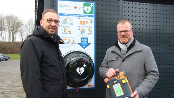 Mike Wittsieker (links) von der Verwaltung und B&uuml;rgermeister Friso Veldink stehen vor einem der neuen Defibrillatoren, der au&szlig;en am Gel&auml;nde des Rathauses angebracht ist. - &copy; Nadine Uphoff