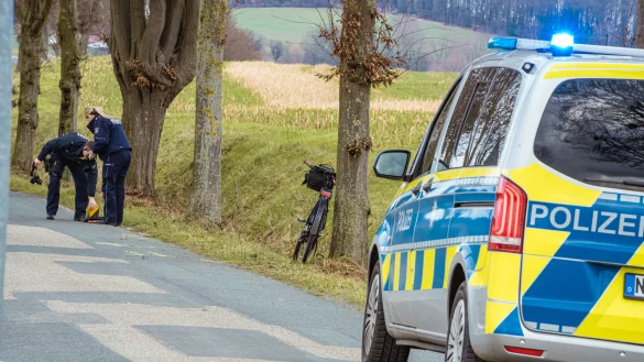 Beamte messen die Unfallstelle an der Breder Straße aus. Das E-Bike des Lagensers lehnt an einem Baum. - © FREITAG-TV