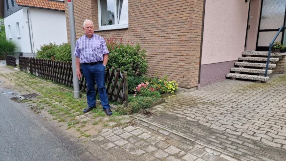 Kurt Hagemeyer steht neben seiner Hofzufahrt. Zwischen der schmalen Stra&szlig;e und seinem Grundst&uuml;ck gibt es einen Streifen mit Pflastersteinen. Dort wurden nach den Glasfaserarbeiten einfach kleine Mosaiksteine eingesetzt, statt der gro&szlig;en Pflastersteine. Die Folge: Ein Kante, die f&uuml;r seine Frau, die auf einen Rollator oder Kr&uuml;cken angewiesen ist, eine Gefahr sein kann. Auch der Zaun (hinten links) wurde bei den Arbeiten dreckig. - &copy; Nadine Uphoff