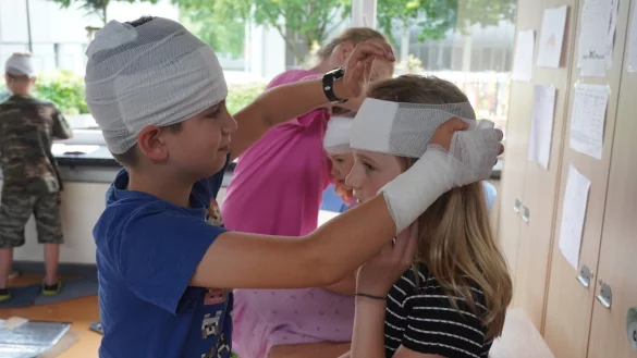 Adrian (10) legt seiner Mitsch&uuml;lerin Mia (10) einen Kopfverband an. Wegen ihrer langen Haare ist das gar nicht so einfach, doch der Erste Hilfe-Trainer hat daf&uuml;r einen Tipp parat. - &copy; Michaela Wei&szlig;e