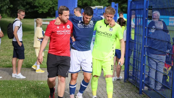 Gerrit Gohlke wird von Physiotherapeut Arne B&ouml;ker (links) und Torwart Leo Oppermann gest&uuml;tzt, das rechte Sprunggelenk des Abwehrspielers ist bandagiert. - &copy; Oliver Krato