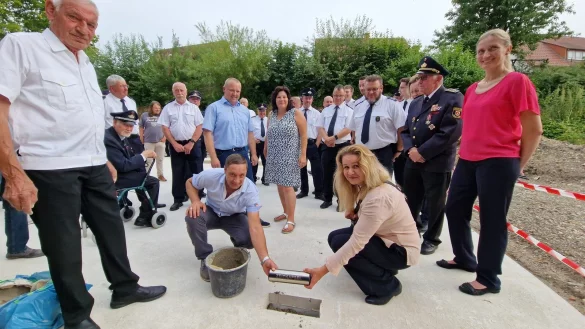 Ewa Hermann und Nicolai Stoll vom Bauamt der Gemeinde Kalletal setzen die Zeitkapsel ins Fundament des neuen Feuerwehrger&auml;tehauses in Talle, w&auml;hrend unter anderem dahinter Uwe Kordfunke (links) aus der Ehrenamtsabteilung der Feuerwehr, B&uuml;rgermeister Mario Hecker (hinter Nicolai Stoll), daneben Fachbereichsleiterin Ordnung und Soziales Andrea Batzer sowie Architektin Wera Binder (rechts). - &copy; Nadine Uphoff