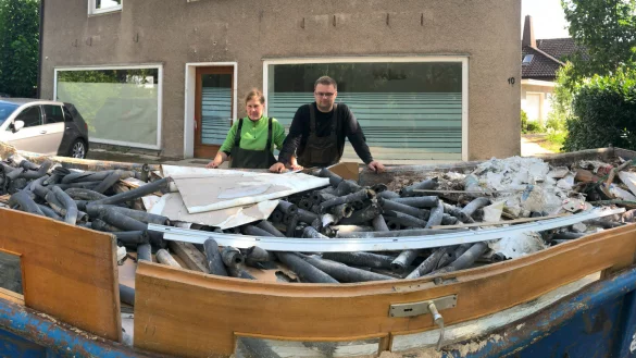Nathalie Witt und Max K&ouml;nig stehen vor einer von vier gro&szlig;en Mulden mit Abfall aus dem vollgelaufenen Keller ihres Hauses (im Hintergrund). - &copy; Thomas Reineke