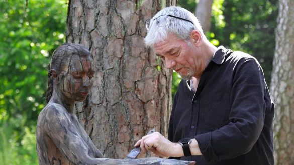 K&uuml;nstler J&ouml;rg D&uuml;sterwald stylt sein Aktmodell Fee so mit K&ouml;rperfarbe, dass die junge Frau mit der Kulisse im Wald verschmilzt. - &copy; Peter Bunn / Atelier J&ouml;rg D&uuml;sterwald