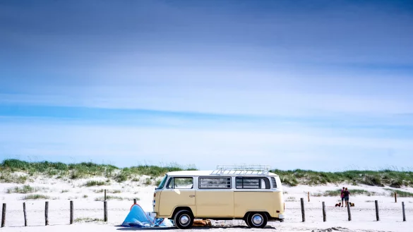 Camper parken mit einem historischen Bulli am Strand und erfüllen sich ihren kleinen Traum vom Glück. - © picture alliance/dpa