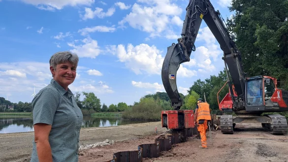 Susanne Hoffmann, stellvertretende Leiterin der Forstabteilung des Landesverbands Lippe, begleitet die Arbeiten am Norderteich. Im Hintergrund bringen Mitarbeiter der Firma Kögel die Spundwandelemente mit schwerem Gerät in den Boden ein. - © Carolin Brokmann-Förster
