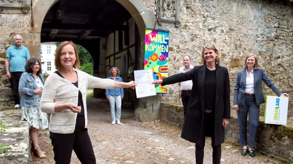 Regierungspr&auml;sidentin Judith Pirscher (2.v.r.) &uuml;berreicht die F&ouml;rderung an die Vorsitzende des Vereins Wasserschloss Reelkirchen, Sigrun Brunsiek (3.v.l.). Neben Mitgliedern des Vereins waren Blombergs B&uuml;rgermeister Christoph Dolle (2.v.r.) und REGIONALE-Leiterin Annette Nothnagel (r) dabei. - &copy; OstwestfalenLippe GmbH