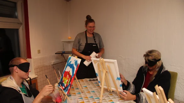 Kasimir Eckhardt und Marion malen, w&auml;hrend sie eine Schlafmaske auf den Augen haben. Leiterin Katharina Wiesner h&auml;lt K&uuml;chenrolle bereit, falls die Kursteilnehmer sich bekleckern. - &copy; Nadine Uphoff