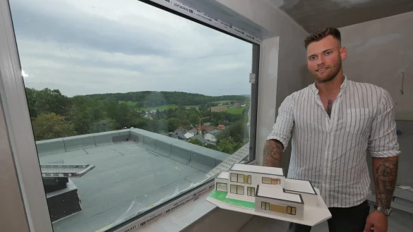 Paul Neudorf baut sich eine ausgewachsene Villa. Das spätere Bad, in dem er steht und ein Modell seines Hauses hält, bekommt ein Panoramafenster für den Blick über den Ortsteil. - © Jost Wolf