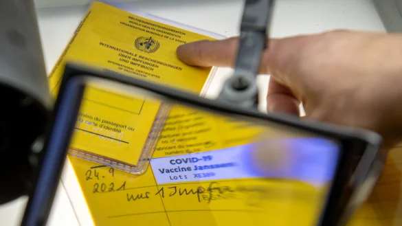 Bei der Kriminalpolizeiinspektion liegen Impfp&auml;sse unter einer Lupe, darunter ein aufgeschlagener Impfausweis. - &copy; Symbolbild: Stefan Puchner/dpa