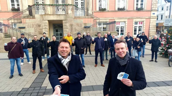 B&uuml;rgermeister Frank Hilker (links) und Round table-Pr&auml;sident Julian Hilker halten die ersten Kartensets des neuen Gastro-Quartetts in den H&auml;nden. Im Hintergrund haben sich viele der beteiligten Gastronomen versammelt. - &copy; Janet K&ouml;nig
